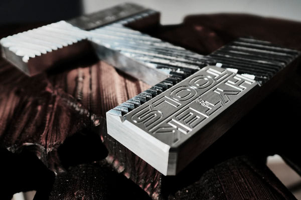 Close-up of the 2024 ROUTEK™ CNC Industrial Router by Hytek Tools, showcasing engraved branding and textured surfaces. It rests on dark, ribbed material with lighting casting intricate shadows that highlight its precision craftsmanship.