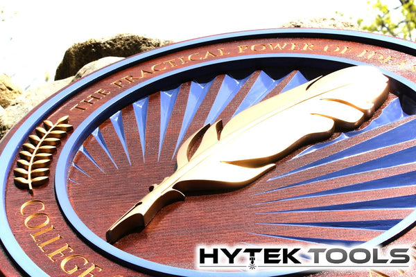 This wooden plaque, showcasing THE PRACTICAL POWER OF INDEPENDENT THOUGHT in a sunburst pattern with a golden quill, exemplifies the precision of the Aspire by Vectric - Version 11.5 CNC router. It sits outdoors, proudly displaying the Hytek Tools logo beneath.
