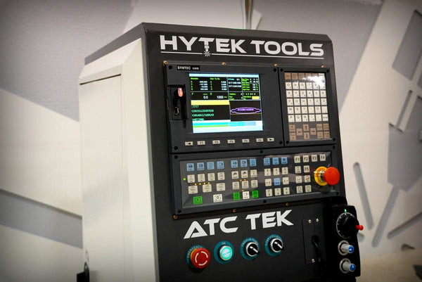 The Hytek Tools control panel for the 2024 ATCTEK™ CNC Industrial Router Machine Pkg features a screen, numerous buttons, knobs, and a large red emergency stop button. It displays data and graphs for operating advanced industrial machinery.