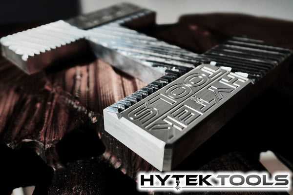 Close-up of the metallic Hytek Tools logo on a textured background. The intricate grooves and raised text highlight the brand, reflecting precision similar to a 2024 ATCTEK™ CNC Industrial Router Machine Pkgs craftsmanship.