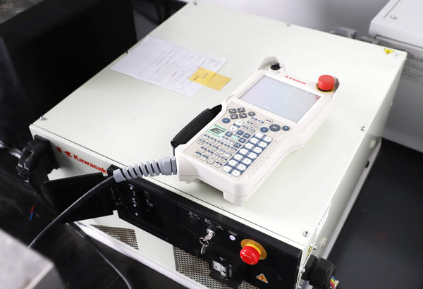 A white control device with a keypad and screen is placed on the Robot Welder - BOTWELD™ 6 Axis Laser Welder from Hytek Tools. The setup, featuring Kawasaki servo drivers, includes buttons, switches, and a coiled cable connecting to the device.